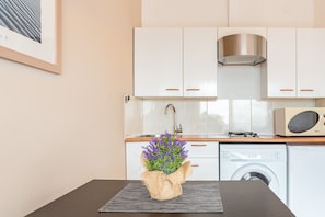 A kitchen with white cabinets, a stainless steel range hood, a microwave, and a washing machine.