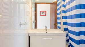 A bathroom with a white sink, a mirror, and a striped shower curtain. - Holiday Home 'Casa Karen' with Sea View, Private Terrace and Wi-Fi (Tossa del Mar)