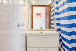 Une salle de bain avec un lavabo blanc, un miroir et un rideau de douche à rayures.