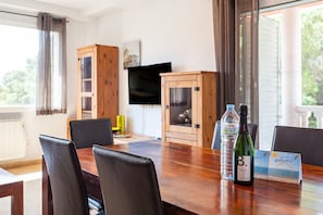 Un comedor con una mesa de madera, sillas, un televisor y una botella de vino.