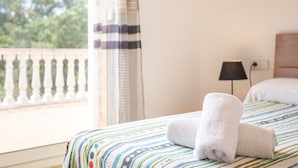A hotel room with a bed, a window with curtains, a lamp, and a view of greenery outside. - Holiday Home 'Casa Martini' with Sea View and Private Terrace (Tossa del Mar)