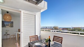 Un área de comedor al aire libre con una mesa preparada para dos personas, una botella de vino y vistas al mar.