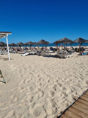 Une plage avec des chaises longues et des parasols en chaume.
