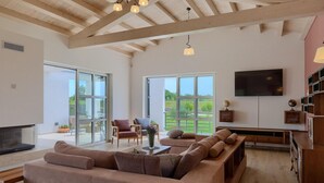 A spacious living room with a large sofa, a television, and a wooden ceiling.