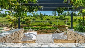 A stone-paved area with a pergola structure and hanging hammocks overlooking a landscaped garden.