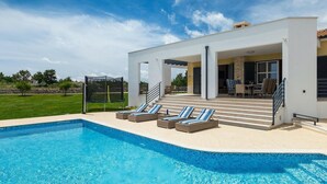 A modern house with a swimming pool, outdoor seating, and a covered patio area.