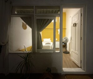 A room with a bed, a bedside table, a fan, and a window with curtains. - Coliving SCZ (Santa Cruz de la Sierra)