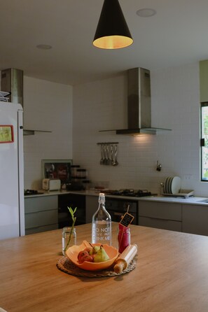 A kitchen with a wooden countertop, a bottle of water, a bowl of fruit, and a hanging light fixture. - Coliving SCZ (Santa Cruz de la Sierra)