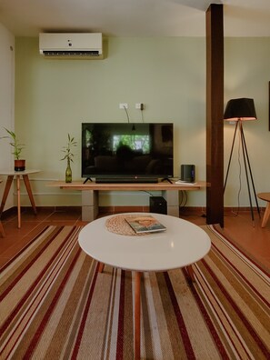 A modern living room with a flat-screen TV, a coffee table, a floor lamp, and two potted plants. - Coliving SCZ (Santa Cruz de la Sierra)