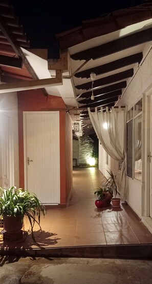 A covered outdoor corridor with potted plants, a white door, and a tiled floor. - Coliving SCZ (Santa Cruz de la Sierra)