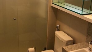 Un baño con inodoro, lavabo y repisa de vidrio sobre el lavabo.