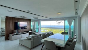 Una sala de estar moderna con un televisor de pantalla plana grande, un comedor con mesa de vidrio y vistas al exterior.