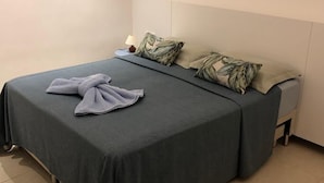 Una cama bien hecha con un edredón gris, dos almohadas con estampado de hojas y una toalla doblada sobre la cama.