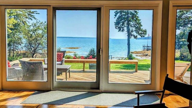 A room with a large sliding glass door leading to an outdoor deck with a view of the water.