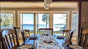 A dining table set for six with chairs, large windows, and a view of the water.