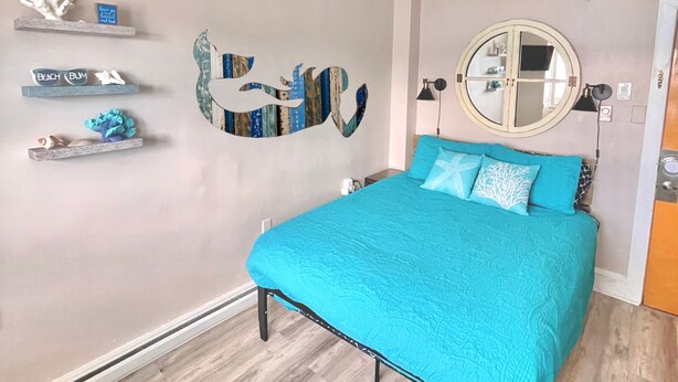 A bedroom with a bed, a ceiling fan, a round mirror, and decorative wall art. - Ocean City, NJ - Feet to the Boardwalk, New Listing, Turnkey & Clean! (Ocean City)