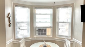 A dining area with a round table and four chairs, a decorative centerpiece, and three bay windows with blinds. - Ocean City, NJ - Feet to the Boardwalk, New Listing, Turnkey & Clean! (Ocean City)