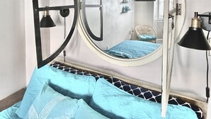 A bedroom with a bed, a round mirror, a door, and a nightstand with a lamp. - Ocean City, NJ - Feet to the Boardwalk, New Listing, Turnkey & Clean! (Ocean City)