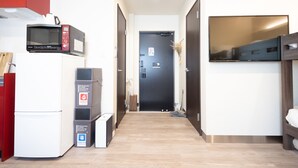 Een kleine hotelkamer met kitchenette, een bed, een televisie en een deur met een bordje.