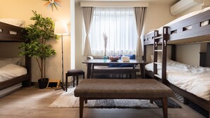 Een compacte hotelkamer met stapelbedden, een eettafeltje, een potplant en een raam met gordijnen.