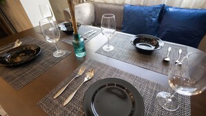Een eettafel gedekt met zwarte borden, bestek en wijnglazen, met een blauwe vaas en een kaars op tafel.