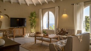 A living room with a TV, sofa, coffee table, and a large window with curtains. - Casa Peponi - By Almarina Villas (Javea)