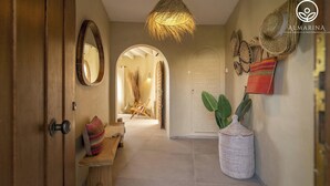 A hallway with a wooden door, a bench with cushions, a woven basket, and a hanging light fixture. - Casa Peponi - By Almarina Villas (Javea)