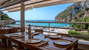 An outdoor dining area with tables set for two, overlooking a beach with people and umbrellas. - Casa Peponi - By Almarina Villas (Javea)