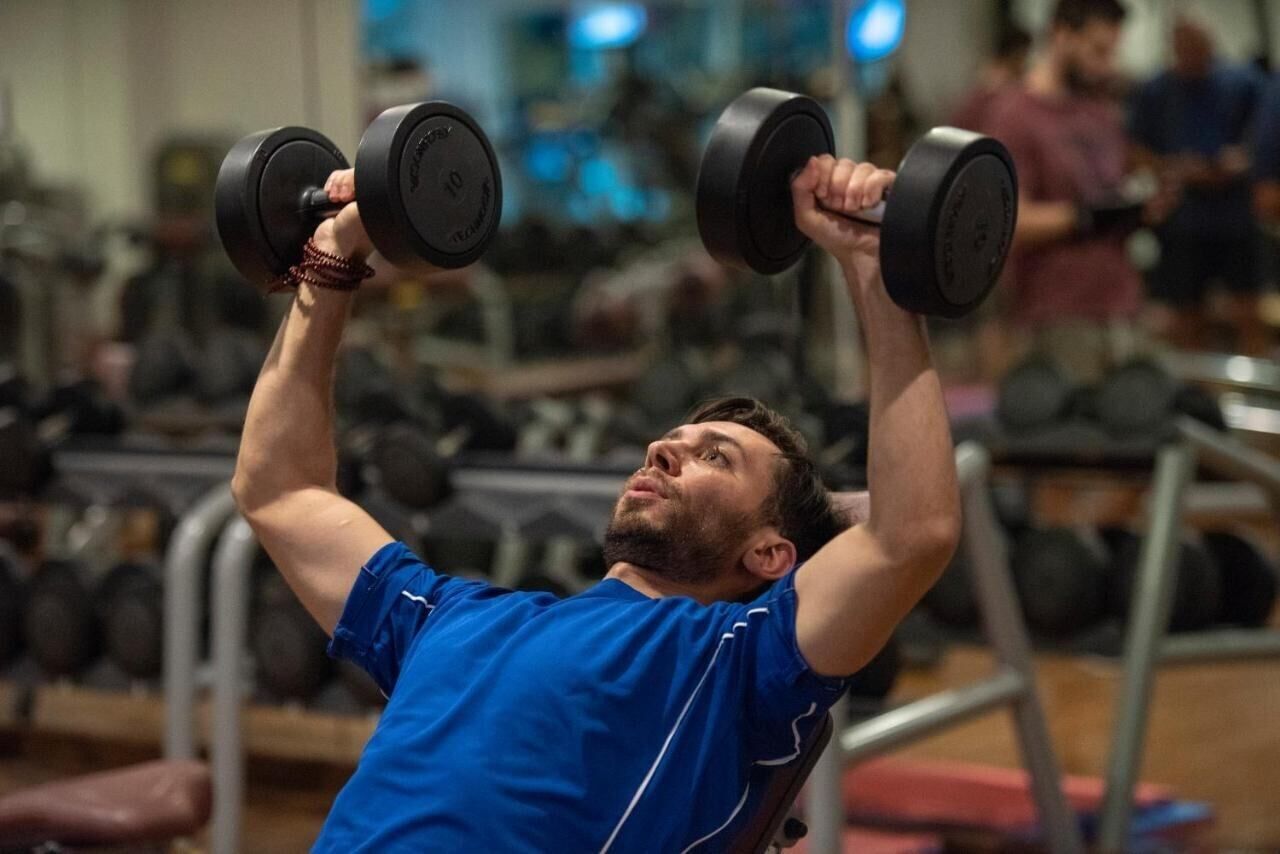 A person lifting weights in a gym with various equipment in the background.