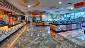 Eine moderne Hotelhalle mit einer zentralen Rezeption, einer Treppe und einem Frühstücksbereich.