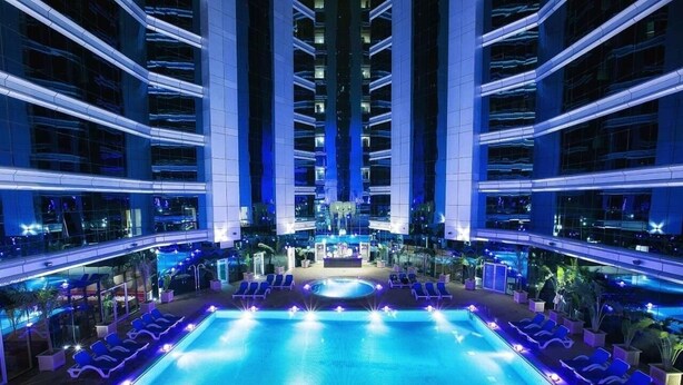 Ein modernes Hotel mit einem zentralen Schwimmbecken, mehreren Balkonen und einem hell erleuchteten Innenhof.