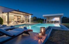 A modern outdoor pool area with lounge chairs, a stone wall, and a dining area with a grill. - Gorgeous home in Medulin (Medulin)