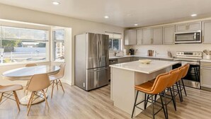 A modern kitchen with a central island, stainless steel appliances, and a dining area with a round table and chairs. - Canyon View Cottage | Backyard | Free Massage* (Provo)