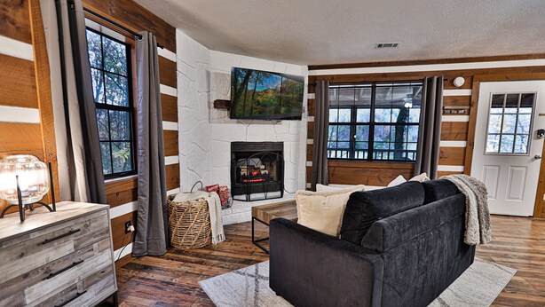 A cozy living room with a fireplace, wooden floors, a sofa, and large windows. - Honeymoon Getaway•Hot Tub•Fireplace•VIEWS•Seclusion (Sevierville)
