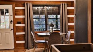 A room with a wooden floor, a round table with chairs, a door, and a window with curtains. - Honeymoon Getaway•Hot Tub•Fireplace•VIEWS•Seclusion (Sevierville)