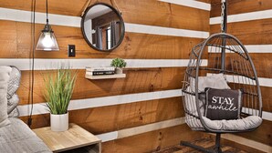 A cozy room with a hanging chair, a small shelf with books and a plant, a bedside table, and a wooden wall with horizontal planks. - Honeymoon Getaway•Hot Tub•Fireplace•VIEWS•Seclusion (Sevierville)
