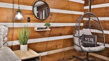 Une pièce chaleureuse avec un fauteuil suspendu, une petite étagère avec des livres et une plante, une table de chevet et un mur en bois avec des planches horizontales.