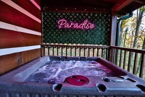 Ein Whirlpool mit einem Neon-Schild mit der Aufschrift „Paradise“ und Blick auf Bäume durch ein Fenster.