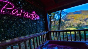A hot tub with a neon sign reading "Paradise" and a view of a forested landscape. - Honeymoon Getaway•Hot Tub•Fireplace•VIEWS•Seclusion (Sevierville)