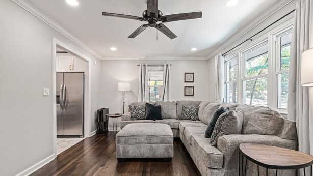 A modern living room with a sectional sofa, a small round table, and a ceiling fan. - Modern 3BR Home Near LakePoint with Fenced Yard (Cartersville)
