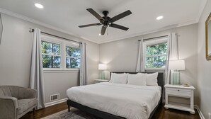 A bedroom with a bed, two bedside tables, a chair, a ceiling fan, and windows with curtains. - Modern 3BR Home Near LakePoint with Fenced Yard (Cartersville)