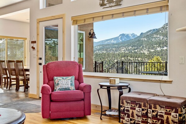 Une pièce dotée d’une grande fenêtre donnant sur les montagnes, d’un fauteuil rouge, d’une petite table ronde et d’un banc agrémenté d’un coussin à motifs.