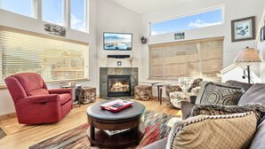 A spacious living room with a fireplace, comfortable seating, and large windows.