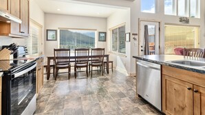 A modern kitchen with a dining area, large windows, and a dishwasher.