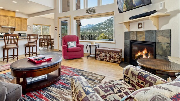 A spacious living room with a fireplace, large windows, and a view of mountains.
