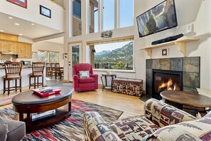 Un salon spacieux doté d’une cheminée, de grandes fenêtres et offrant une vue sur les montagnes.