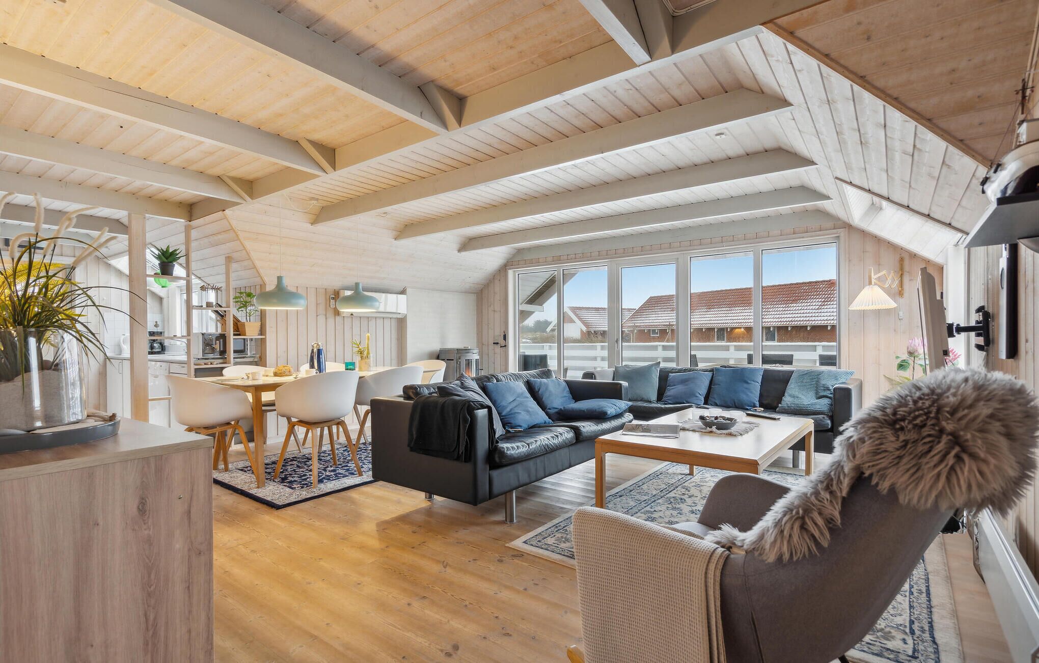 A spacious loft with high ceilings, a dining area, a living room with a sofa and a dog, and large windows offering a view of the neighborhood.