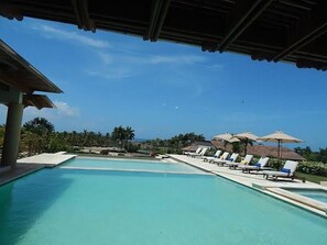 A clear blue pool with lounge chairs and umbrellas, surrounded by palm trees and a view of the ocean. - "Among the Top 10 Exquisite Villas in Casa de Campo" (La Romana)