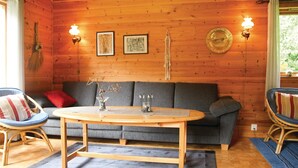 A cozy room with a wooden wall, a grey sofa, a round wooden table, and two wicker chairs. - Amazing home in Sandeid with lake view (Sandeid)