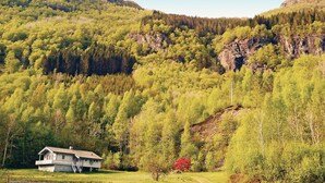 A house with a sloped roof and a balcony, surrounded by a forested hillside. - Amazing home in Sandeid with lake view (Sandeid)